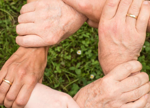 An image of three peoples hands linked together holding each other by the wrist